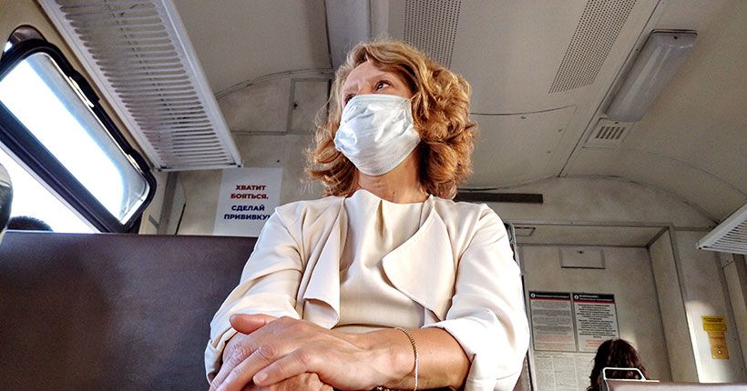 Женщина в маске сидит в электричке на фоне плаката о вакцинации