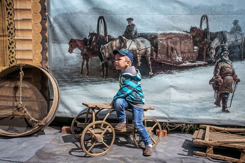 Ребенок сидит на экспонате в музейном дворике Колывани