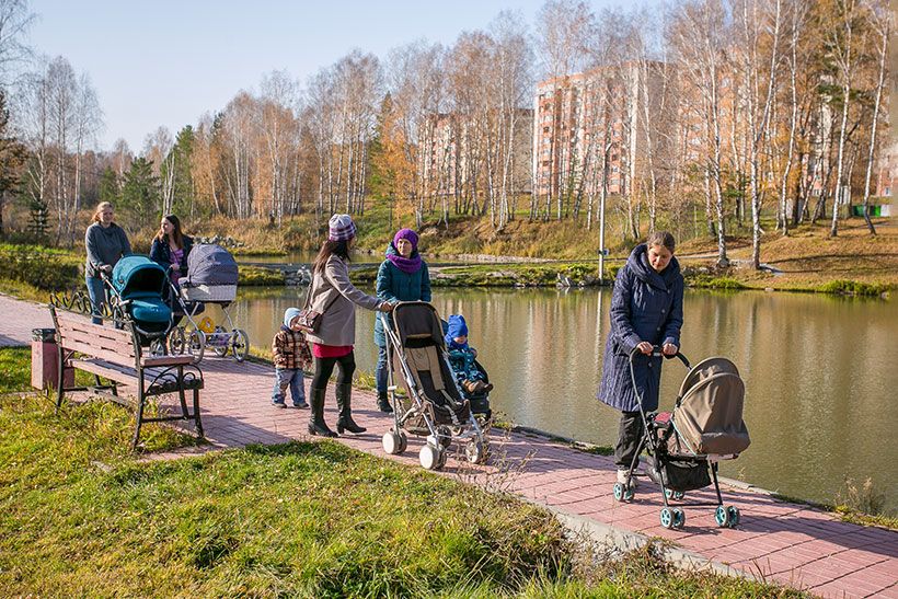 Мамы гуляют с дети в колясках рядом с прудом
