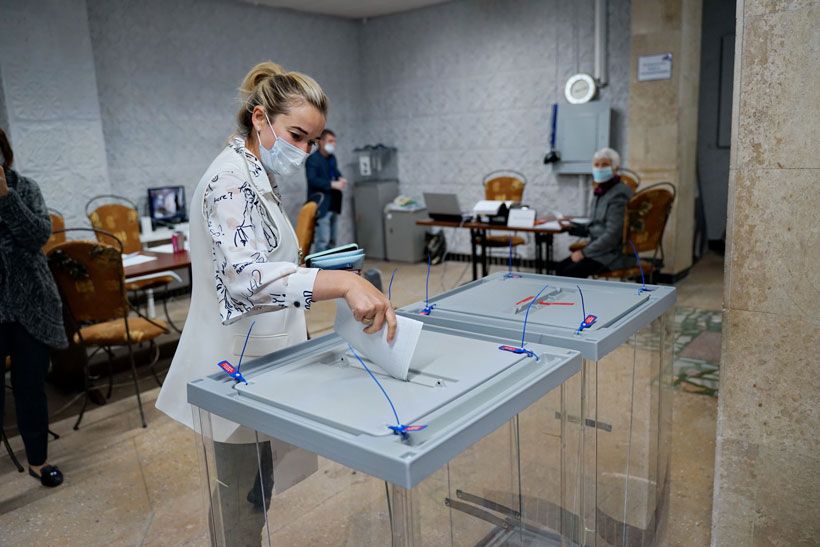 Девушка бросает бюллетень в избирательную урну