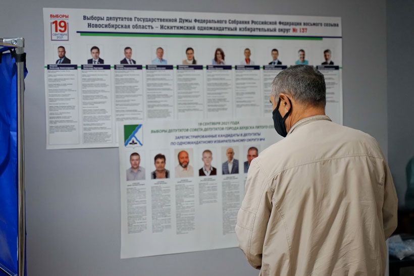 Мужчина в маске перед плакатом с кандидатами в госдуму