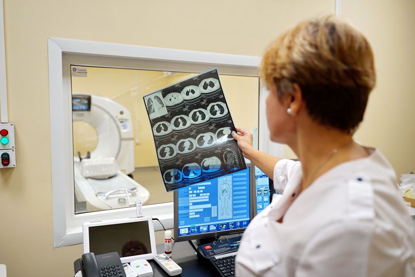 Сотрудница института терапии разглядывает томограмму пациента на фоне томографа